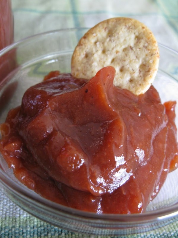 A cracker dipped into a small bowl of smooth apple butter.