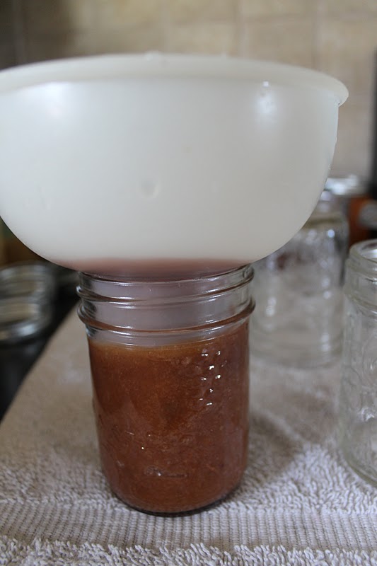 Apple butter in a funnel going into glass jars. 