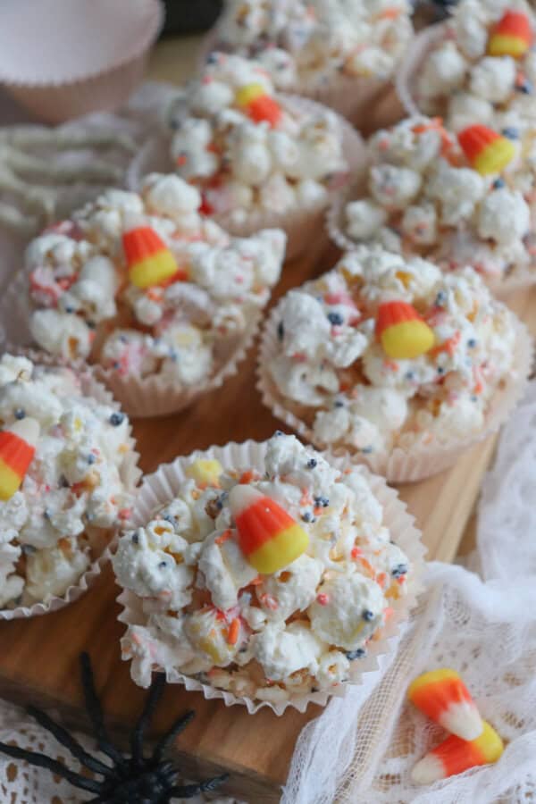 Popcorn balls with Halloween sprinkles and candy corn in cupcake liners on a wooden cutting board.