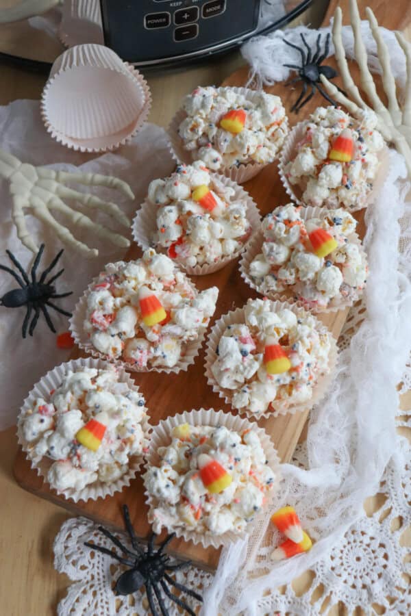 Popcorn balls with Halloween sprinkles and candy corn in cupcake liners on a wooden cutting board.