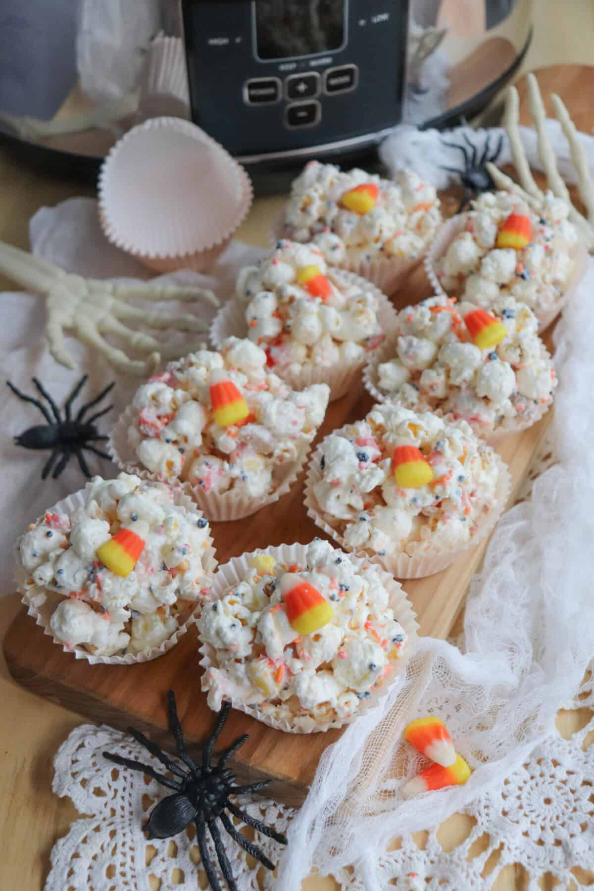 Popcorn balls with Halloween sprinkles and candy corn in cupcake liners on a wooden cutting board.