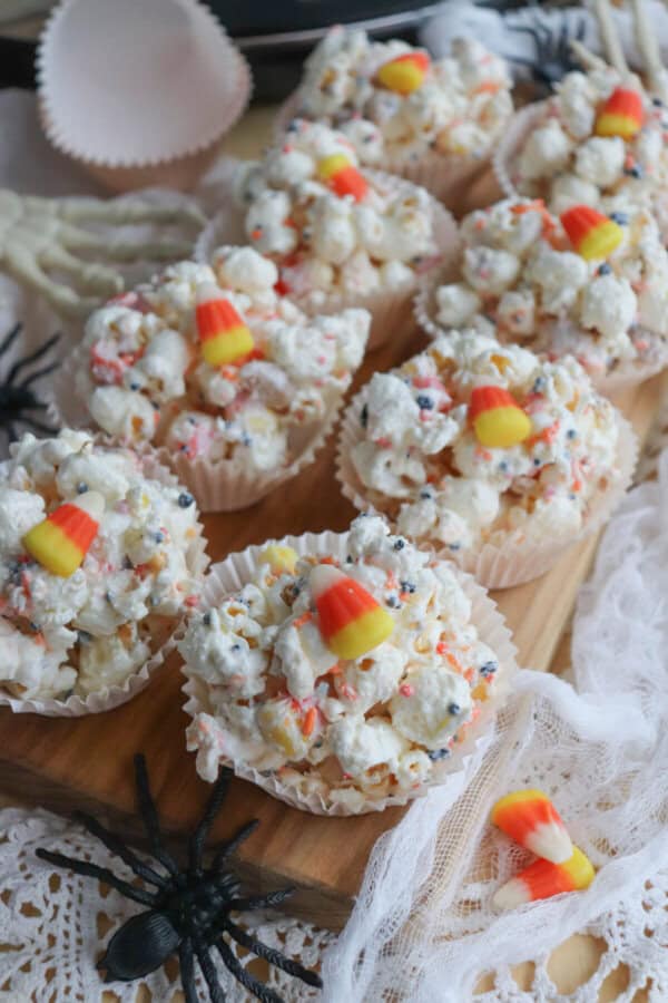 Popcorn balls with Halloween sprinkles and candy corn in cupcake liners on a wooden cutting board.