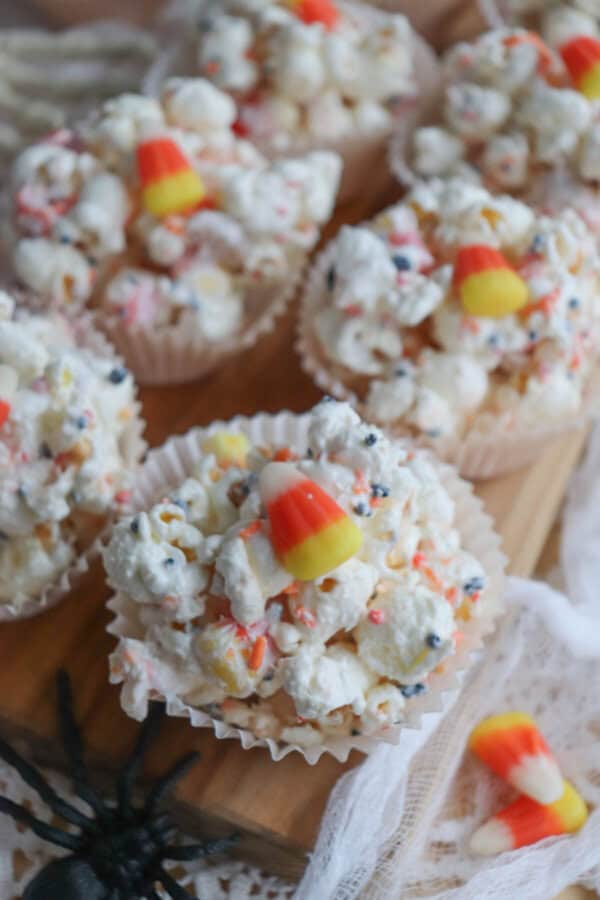 Popcorn balls with Halloween sprinkles and candy corn in cupcake liners on a wooden cutting board.