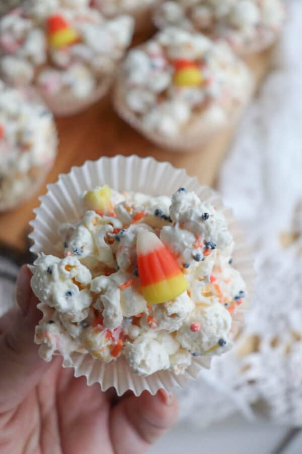 Popcorn balls with Halloween sprinkles and candy corn in cupcake liners on a wooden cutting board.