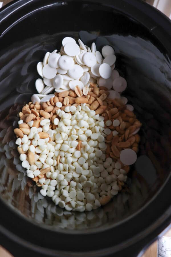 Ingredients for candy corn popcorn in a black crock pot.