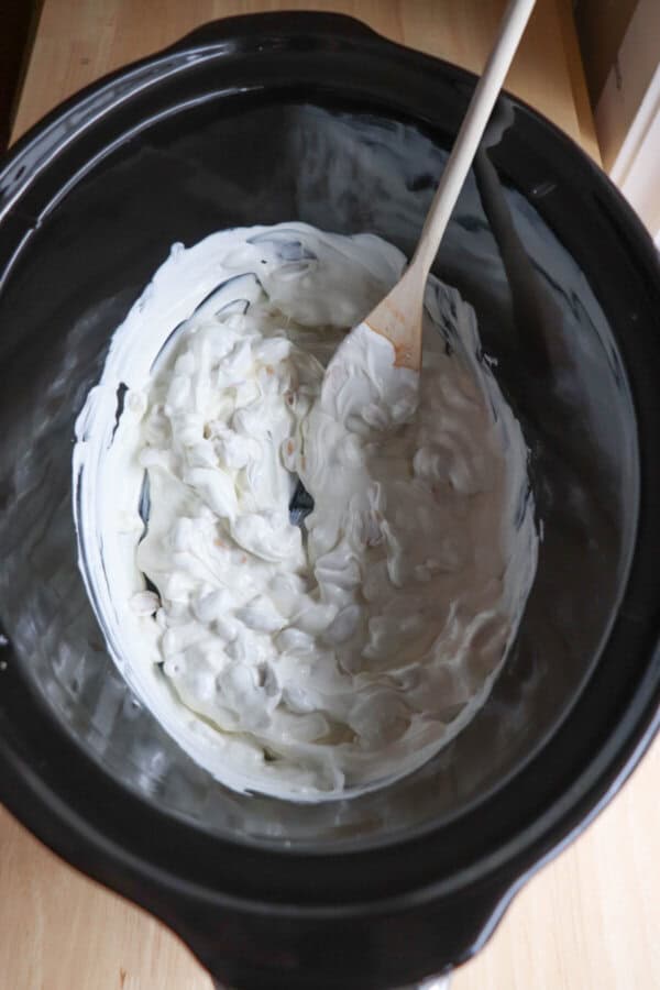 Melted white chocolate and peanuts mixed in a black crock pot.