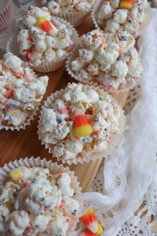 Popcorn balls with Halloween sprinkles and candy corn in cupcake liners on a wooden cutting board.