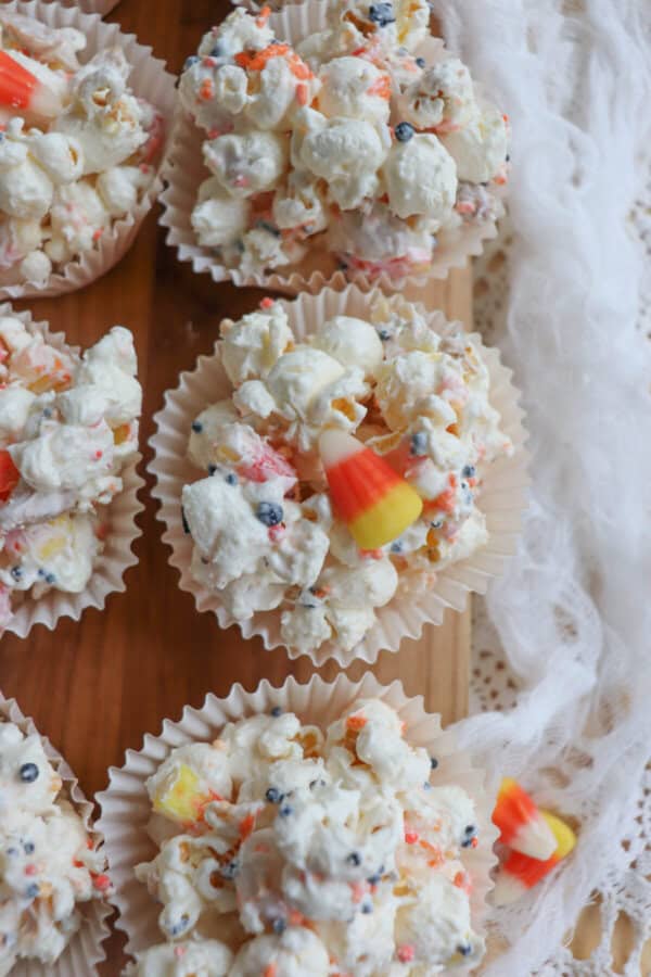 Popcorn balls with Halloween sprinkles and candy corn in cupcake liners on a wooden cutting board.