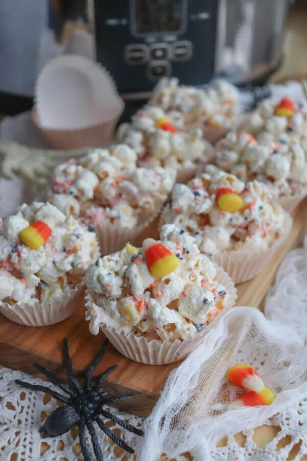 Popcorn balls with Halloween sprinkles and candy corn in cupcake liners on a wooden cutting board.