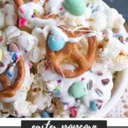 A bowl of Easter snack mix featuring popcorn, pretzels, and colorful candies coated in white chocolate. Alongside, a label reads Easter Popcorn Snack Mix. Perfectly paired with indulgent chocolate coconut date bars for a delightful spring treat. Visit our website for more.