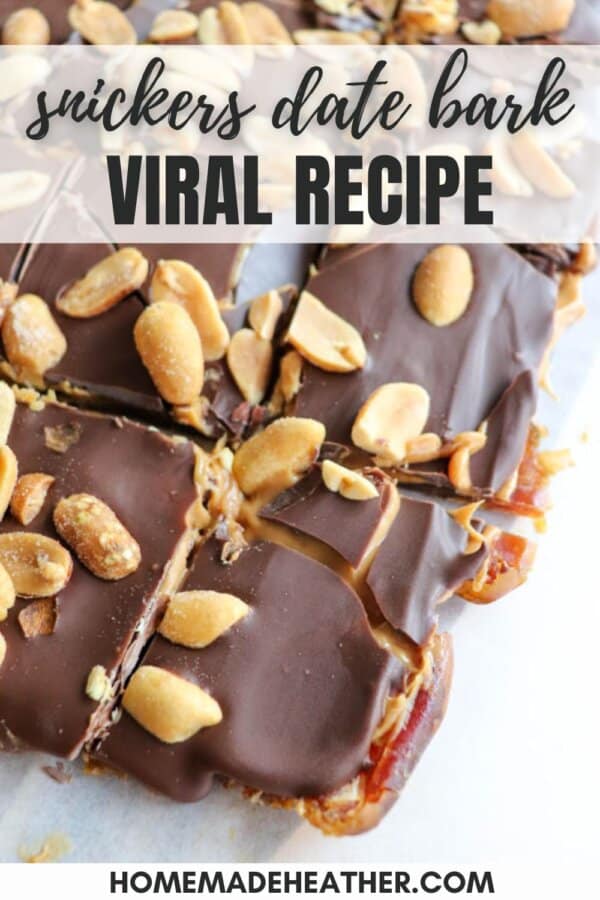 Close-up of chocolate Snickers date bark topped with peanuts. The bark is cut into pieces and placed on parchment paper. Text overlays read, Snickers Date Bark Viral Recipe and homemadeheather.com.