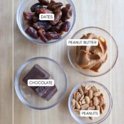 Four bowls on a wooden surface hold ingredients for chocolate coconut date bars, labeled as dates, peanut butter, chocolate, and peanuts. The neat arrangement features text overlaid on a light wood background.