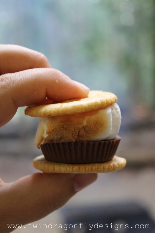 A toasted marshmallow stacked on a reeses peanut butter cup in between two ritz crackers.