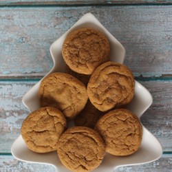 A top view of seven chewy gingersnap cookies arranged in a tree-shaped ceramic dish. The dish is placed on a rustic blue wooden surface, and the cookies have a light brown color with a textured surface.