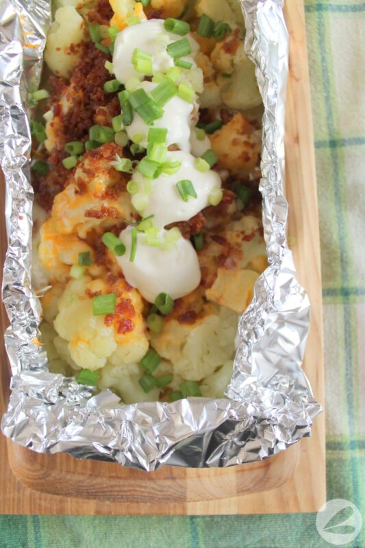 Cooked cauliflower topped with cheddar cheese, bacon bits, sour cream and diced green onions in a foil packet.