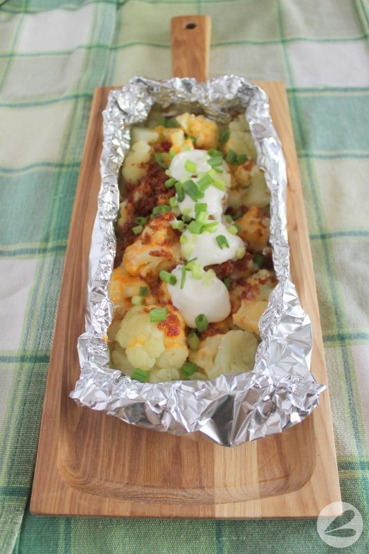 Cooked cauliflower topped with cheddar cheese, bacon bits, sour cream and diced green onions in a foil packet.