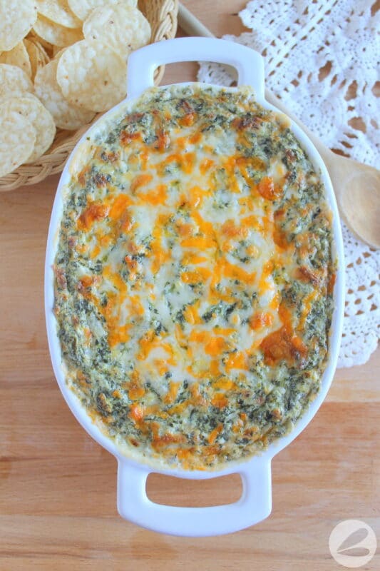 Spinach dip with cheese in a baking dish on a wooden surface.