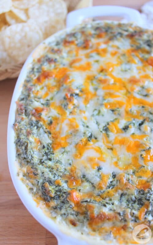 A casserole dish filled with a baked spinach dip recipe and topped with cheese.