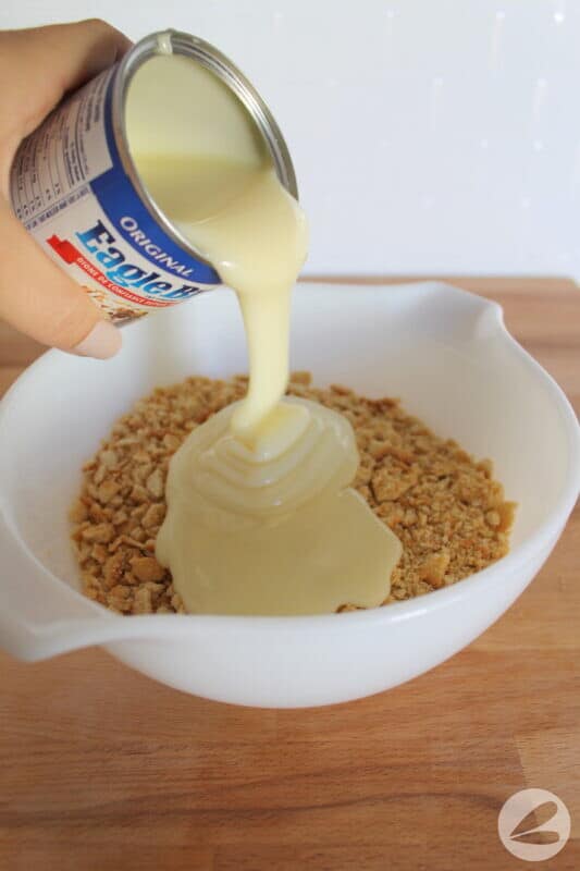 Pouring sweetened condensed milk onto crushed crackers.