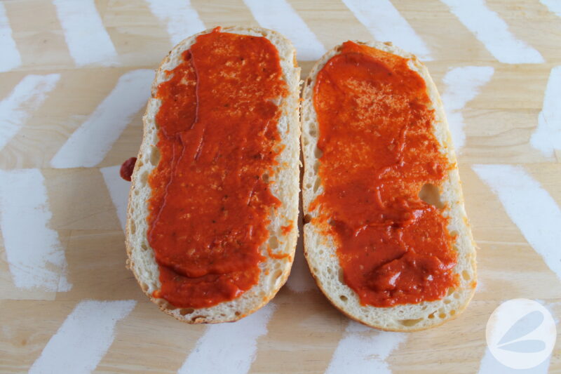 French loaf of bread cut in half and laid open with pizza sauce covering it.