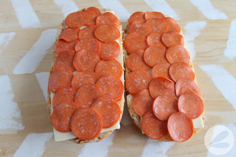 French loaf of bread cut in half and laid open with pizza sauce and pepperoni slices covering it.
