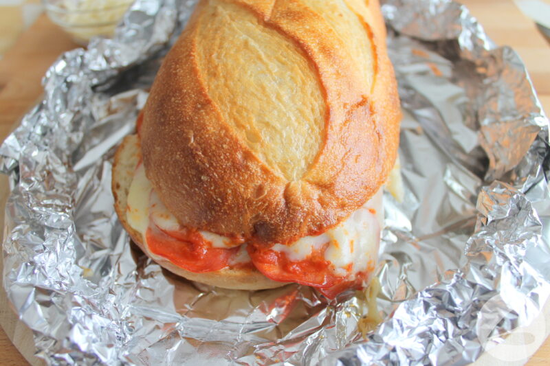 French loaf of bread on foil with pizza sauce, pepperoni slices and mozzarella cheese melting out around the edges.