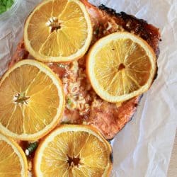 Salmon filet cooked with an orange glaze and thinly sliced oranges on top of a piece of parchment paper.