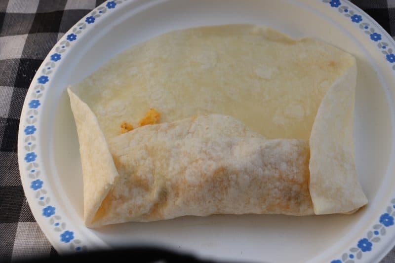 White flour tortilla half folded over cooked scrambled eggs and sausage to form a camping breakfast burrito.