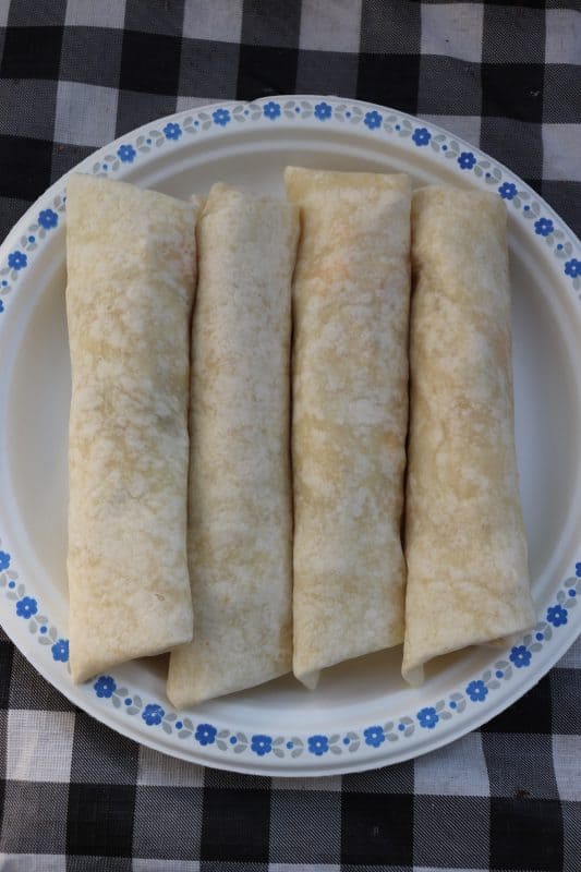 Four camping breakfast burritos on a white paper plate.