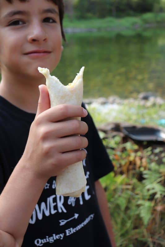Child holding a camping breakfast burrito with a bite taken out of it.