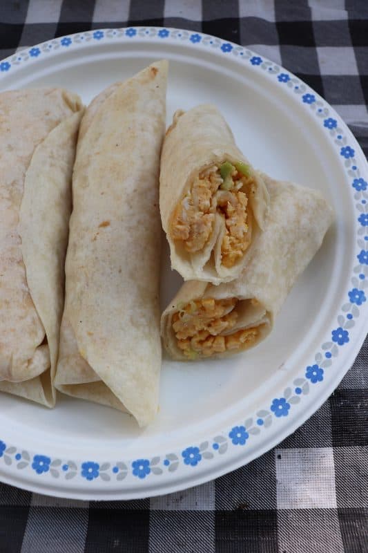 Three breakfast burritos on a paper plate with one cut open to show filling inside.