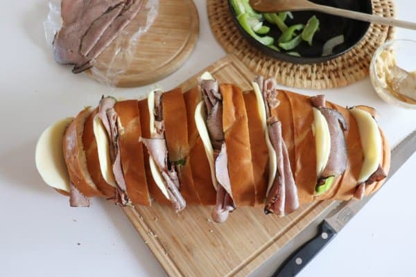Loaf of french bread with 1" slices filled with strips of green bell peppers, roast beef and white cheese.
