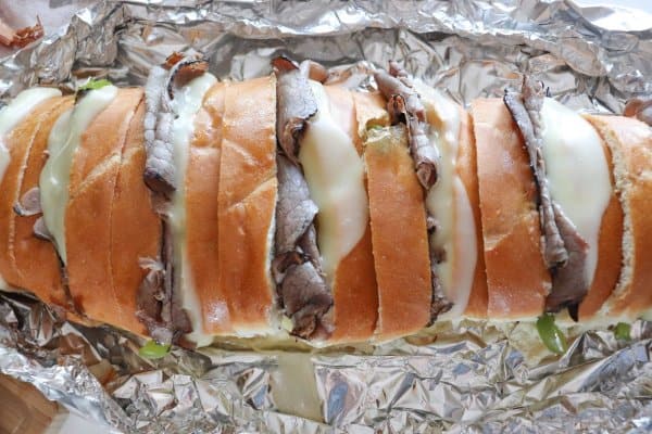 Campfire Philly Cheesecake Sandwich on foil with green bell pepper, roast beef and melted white cheese between slices of french bread.