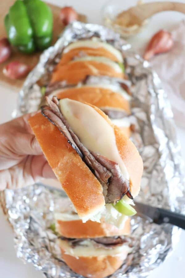 Campfire Philly Cheesecake Sandwich with roast beef and cheese falling out the center held in a hand.