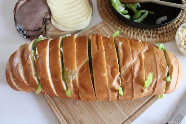 Loaf of french bread with 1" slices filled with strips of green bell peppers.