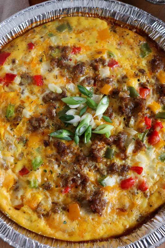 Close up of foil packet breakfast bake with egg, sausage and diced vegetables in a foil pie plate topped with diced green onions.