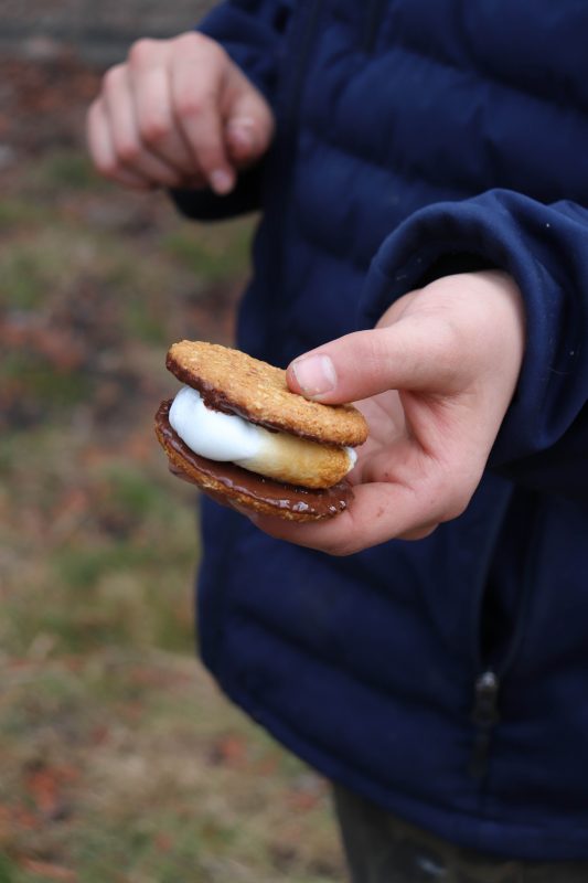 Toasted marshmallow between two chocolate covered cookies held in a childs hand.