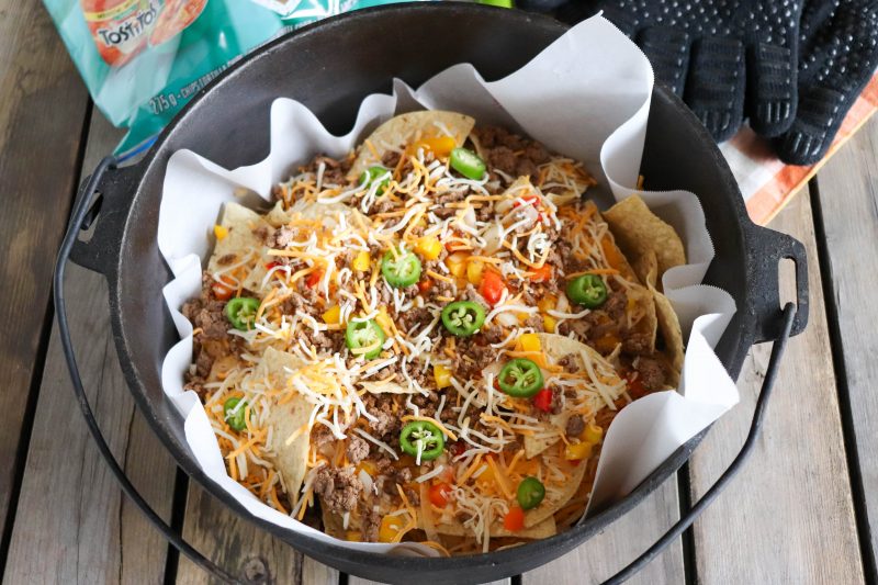 Nachos with ground beef, shredded cheese and diced vegetables in a dutch oven ready to go on the campfire.