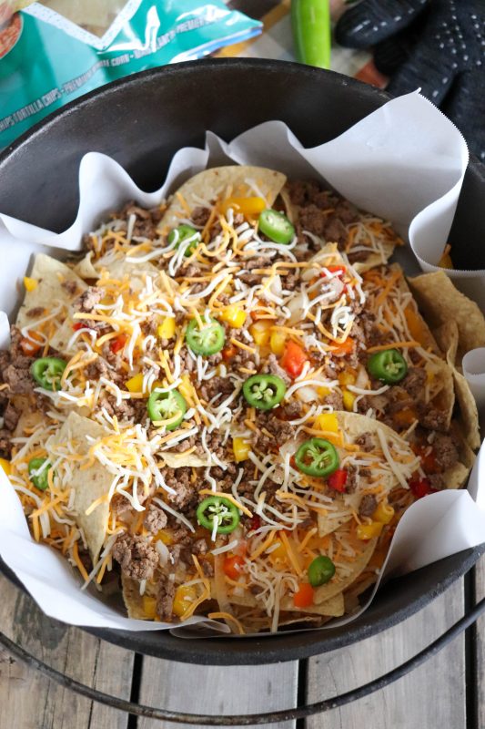 Nachos with ground beef, shredded cheese and diced vegetables in a dutch oven ready to go on the campfire.