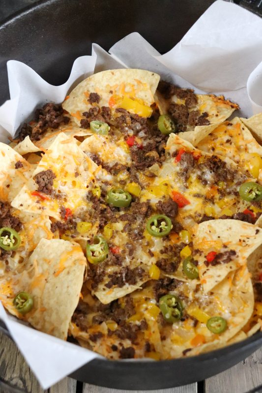 Nachos with ground beef, melted cheese and diced vegetables in a dutch oven lined with parchment paper.