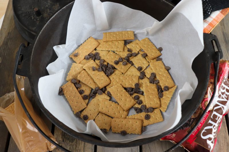 Graham crackers and chocolate chips layered in the bottom of a parchment paper lined dutch oven.