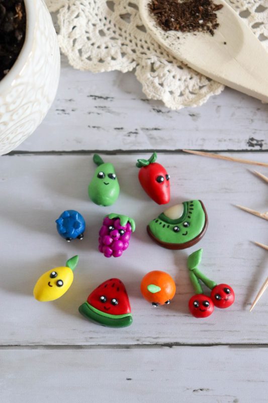 Polymer clay fruit plant markers laying on a white surface.