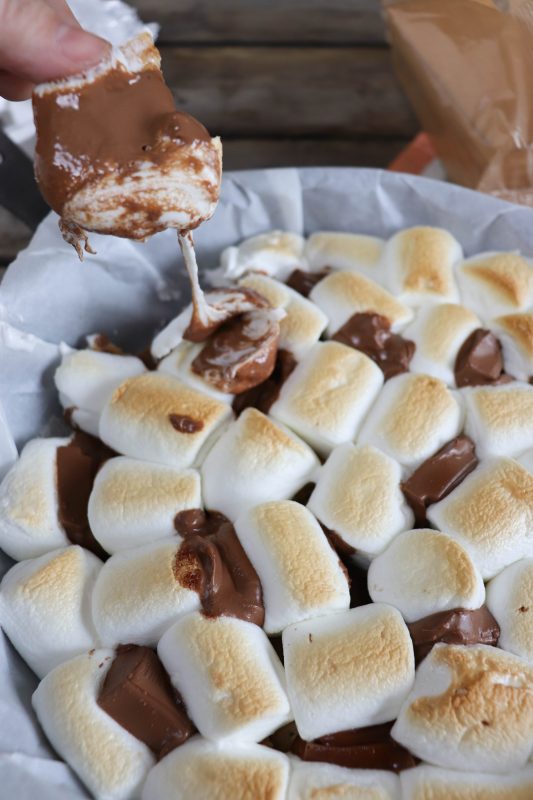 Skillet smores, toasted marshmallows surrounded by melted chocolate in a parchment paper lined skillet.