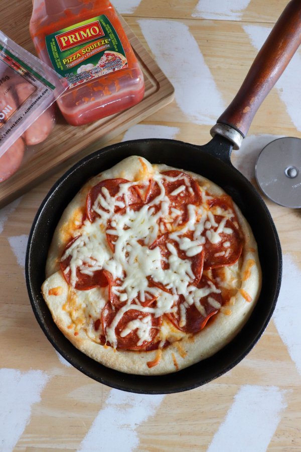 Skillet pizza with tomato sauce, mozzarella cheese and pepperoni slices in a cast iron skillet on a wooden table.