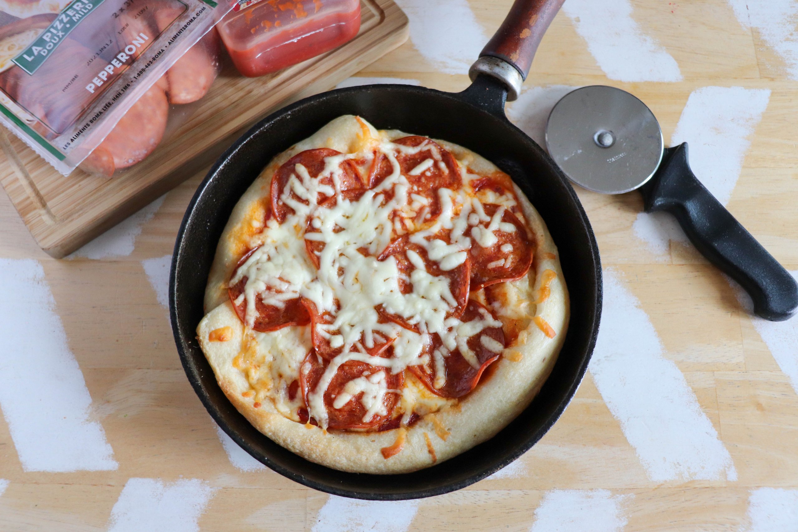 Skillet pizza with tomato sauce, shredded mozzarella and pepperoni slices in a cast iron skillet on a wooden table.