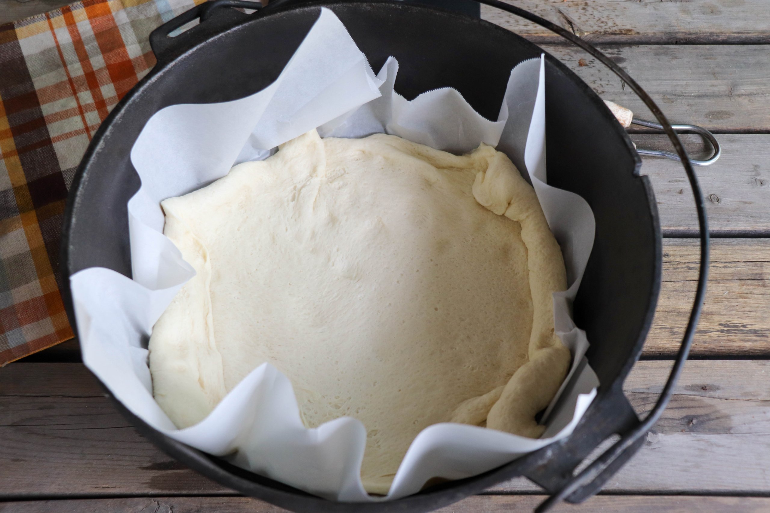 Pizza Dough pressed into the bottom of a parchment paper lined cast iron dutch oven.