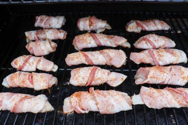 Bacon wrapped chicken tenders are cooking on a grill.