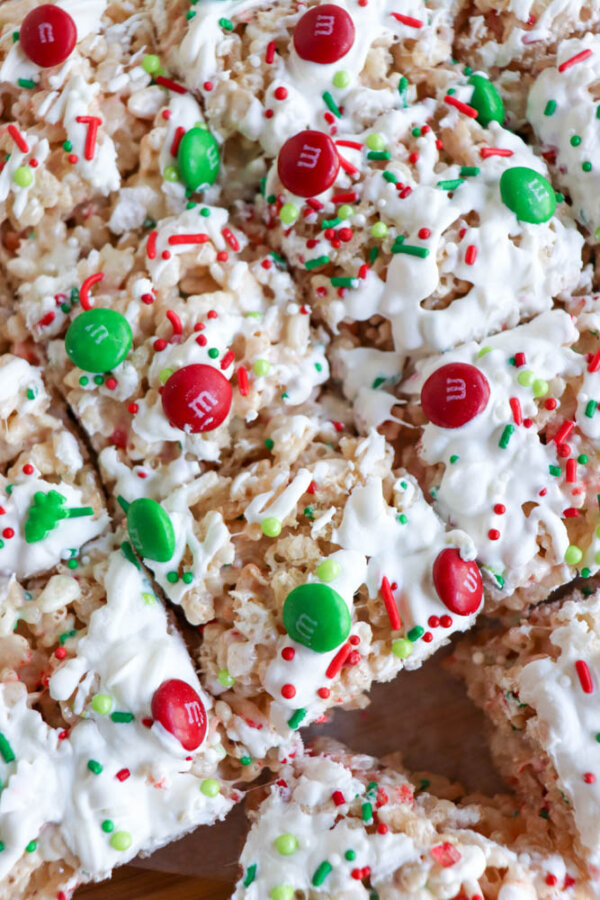 Close-up of festive Christmas Rice Krispie treats topped with white icing, red and green M&M candies, and red, green, and white holiday-themed sprinkles.