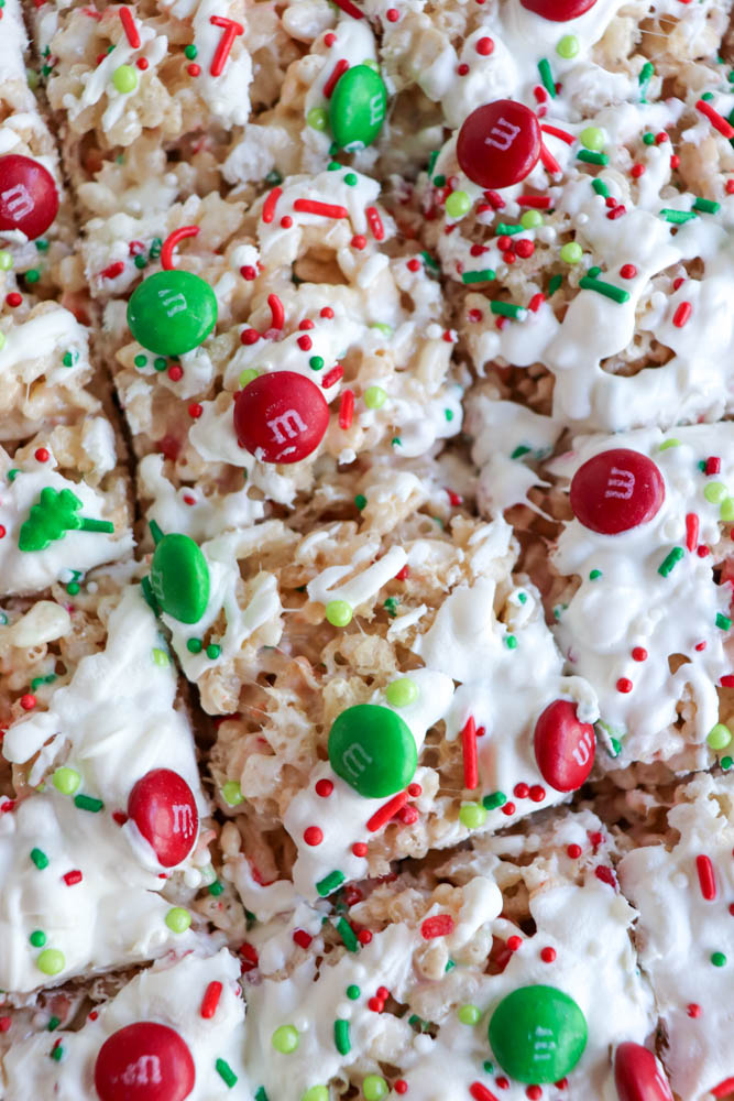 Close-up of Christmas Rice Krispie treats topped with white icing, red and green M&M candies, and festive red, green, and white holiday sprinkles, cut into cheerful squares.