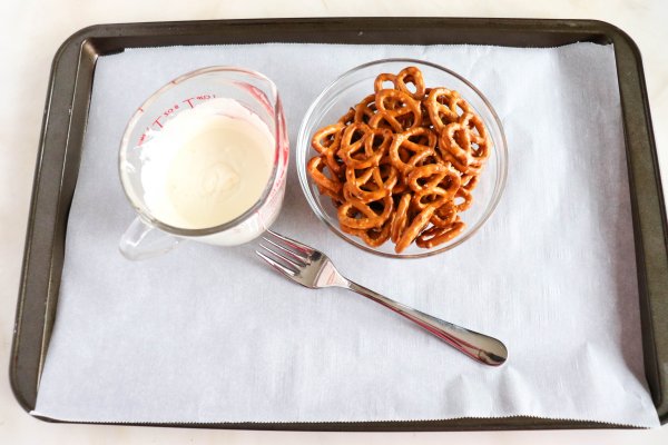 Melted white chocolate and pretzels on a tray with a fork.